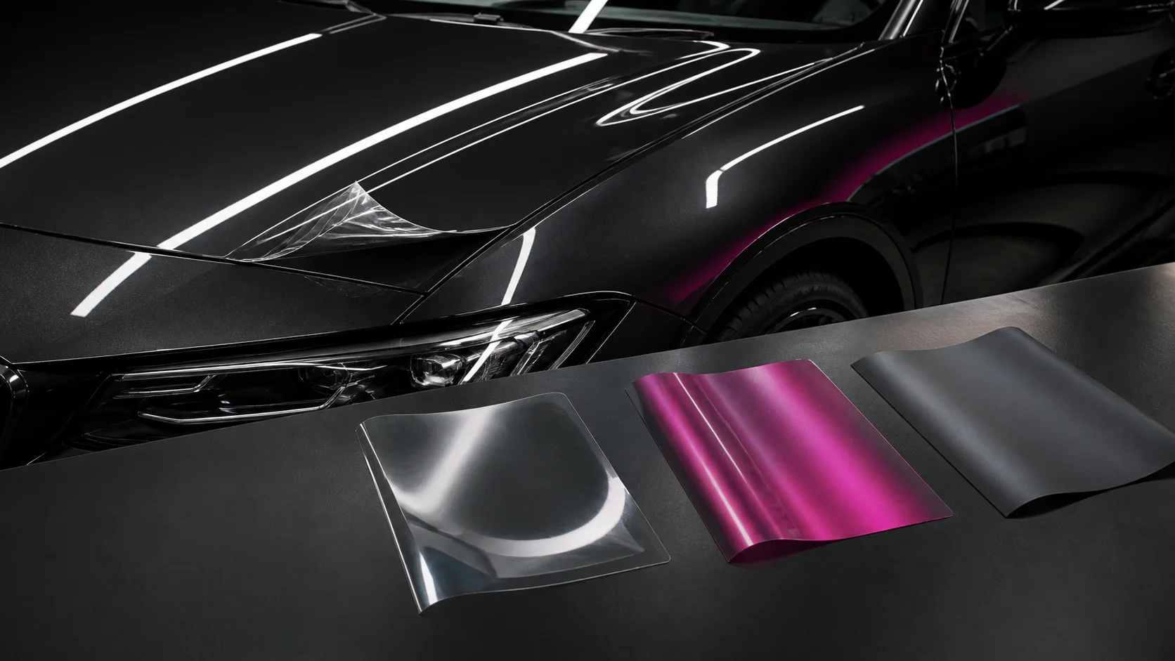 Transparente, satin-magenta und graphitfarbene Folienmuster neben einem Fahrzeug
